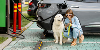 A woman and a dog are sitting next to an electric car being charged