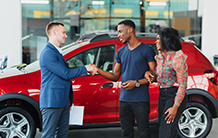 A man is shaking hands with a couple in a car showroom